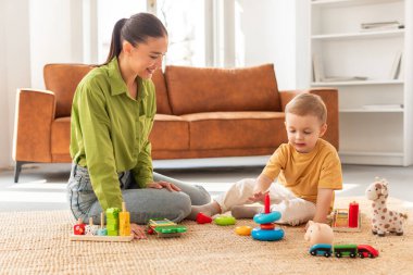 Bir kadın yerde oturuyor, birlikte oynayarak bir çocukla meşgul oluyor. Kapalı bir ortamda birbirlerine eşlik etmek hoşlarına gidiyor gibi..