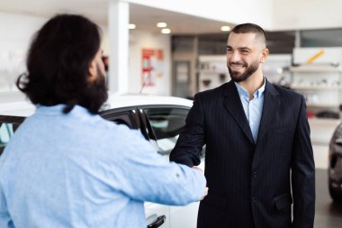 İki adam bir araba galerisinde el sıkışırken, biri günlük giysiler içinde, diğeri de iş elbisesi giymiş, görünüşe göre bir anlaşma ya da anlaşma yapmışlar..