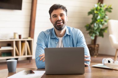 Bir adam dizüstü bilgisayarın önünde oturuyor, klavyeye yazıyor ve ekrana bakıyor. Odaklanmış ve işine dalmış görünüyor..