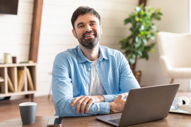 Masada oturan bir adam dizüstü bilgisayarın karşısında ciddi bir ifadeyle oturuyor. Klavyeye yazı yazıyor, görünüşe göre işine ya da elindeki işe odaklanmış..