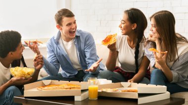 Dört genç arkadaştan oluşan neşeli bir grup, rahat bir oturma odasında toplanmış pizza dilimlerinin tadını çıkarıyor ve neşeli bir sohbete dalıyorlar.