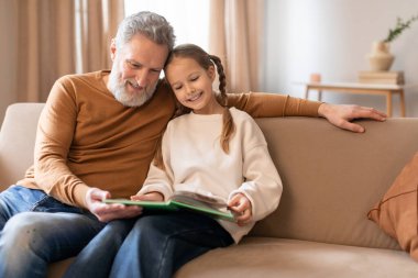 Sıcak ve hassas bir sahne, gri saçlı ve pas rengi gömlekli bir büyükbabanın beyaz bir kazak giyip yeşil bir kitaptan bir hikayeyi paylaşarak torununun yanına oturması gibi..