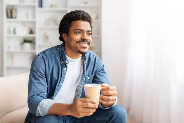 Der Afroamerikaner Sitzt Auf Einer Couch Hält Eine Tasse Kaffee Stockfoto