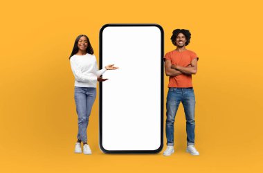 Gülümseyen bir Afro-Amerikan çifti, büyük boyutlu akıllı telefon modelinin boş ekranını sunuyor. Bu da onun özelliklerini veya potansiyel içeriğini gösteriyor.