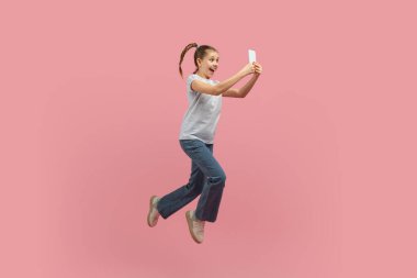 A young girl is captured mid-air, jumping energetically with a cell phone in hand. She appears joyful and carefree as she leaps into the sky with a mobile device. clipart
