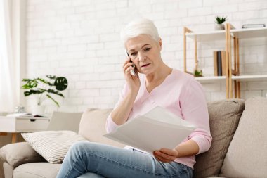 Son sınıf öğrencisi bir kadın evde bir kanepede rahatça oturuyor ve bir telefon görüşmesi yapıyor. Kulağına bir cep telefonu dayamış ve konuşmaya odaklanmış görünüyor..