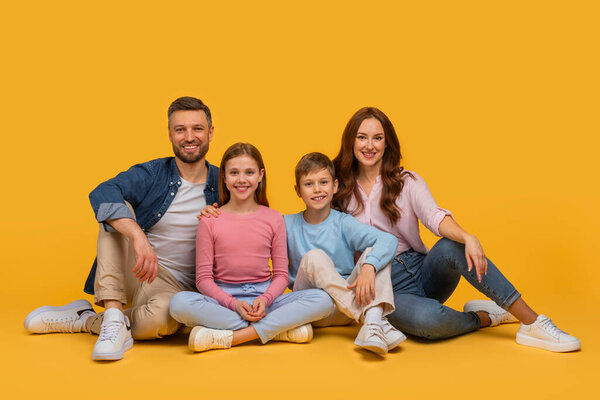 A family consisting of parents and children sitting on the floor, arranging themselves in a pose for a photograph. They are smiling and looking towards the camera.