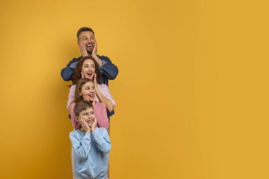 Şaşırmış dört kişilik aile, iki çocuk ve aileleri, dikey olarak dizilmiş, her biri ellerini yanaklarına koyuyor sürpriz ve mutluluk dolu bir ifadeyle, kopyalama alanı