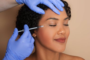 Bir kadın yüz derisine enjeksiyon tedavisi görüyor. İğne, yüzündeki kırışıklıkları ve ince çizgileri azaltmak için eğitimli bir profesyonel tarafından yapılıyor..