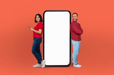 Çok ırklı bir çift dev, boş bir akıllı telefon ekranının her iki tarafında duruyor, hem gülümsüyor hem de boş ekranla meşgul oluyorlar.