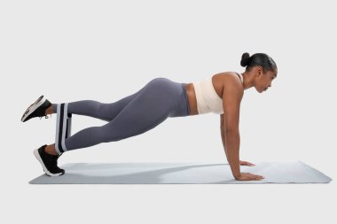 Afrikalı Amerikalı bir kadın spor salonunda ya da spor salonunda şınav çekiyor. Üst vücut kaslarını çalıştırırken direnç bandını kullanarak kalas pozisyonunu koruyor.