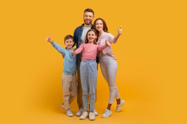Anne, baba, oğul ve kızdan oluşan mutlu bir aile birbirine yakın duruyor, hepsi de işaret veriyor. Canlı sarı bir arkaplanda poz veriyorlar.