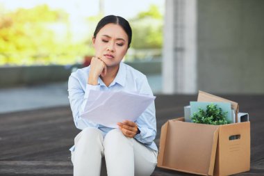 Ofis eşyalarıyla dolu kutusuyla oturan işsiz bir Asyalı kadın. Ekonomiden dolayı işten çıkarıldı.