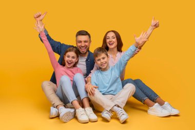 Neşeli bir aile, sevinçle gülümseyen bir kutlama jesti olarak kollarını kaldırarak yan yana oturur. Bir anne ve baba, kızlarının ve oğullarının arkasında, bir anlık mutluluğu paylaşıyorlar.