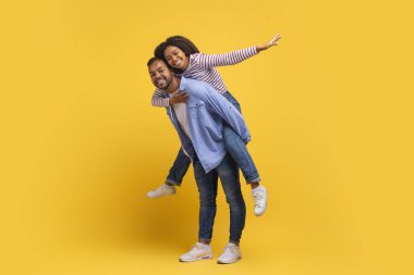 Mutlu bir Afrikalı Amerikalı erkek, neşeli bir kadını sırtında taşır. İkisi de geniş bir şekilde gülümserken kaygısız bir zevk ve şen şakrak bir sevgi gösterir.