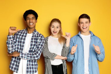 Üç etnik çeşitlilikte genç yan yana duruyorlar, her biri mutlu bir gülümsemeyle ve baş parmak işareti yaparak.