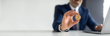 Çevrimiçi Ticaret. Takım Elbiseli İşadamı Masasında oturan ve elinde altın Bitcoin tutan olgun girişimci, ofiste dizüstü bilgisayar kullanan, Kripto Para Madenciliği, Kapanış, Boşluk Kopyalama