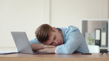 İş yerinde dizüstü bilgisayarda uyuyan yorgun genç adam, evden çalışıyor.
