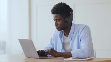 Evde rahat bir iş. Milenyum Afrikalı adam müzik dinliyor ve dizüstü bilgisayarında daktilo yazıyor.