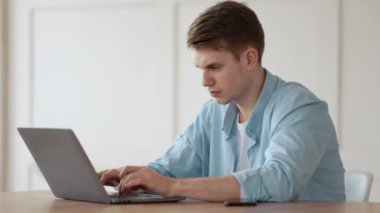 Sistem hatası. Dizüstü bilgisayara bakan, evde çalışmakta zorlanan genç bir adam.