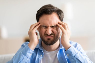 Bir adam elleriyle başını tutuyor, stres ya da sıkıntı belirtileri gösteriyor. İçindeki kargaşayı yansıtan bir yüz ifadesiyle şaşkına dönmüş ya da derin düşüncelere dalmış gibi görünüyor..