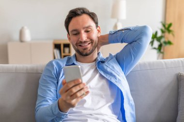 Kanepede oturan bir adam, akıllı telefonuyla meşgul. Ekrandaki aygıtlara odaklanmış durumda, görüntülenen her türlü içeriğe emiliyor..