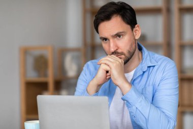 Bir adam dizüstü bilgisayarın önünde oturuyor, derin düşüncelere dalmış, eli çenesinde dinleniyor. Bilgisayarı üzerinde çalışırken bir şey düşünüyor ya da düşünüyor gibi görünüyor..