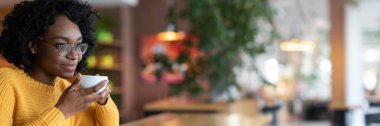 Hayalperest genç siyah bayan kafeteryada bir fincan kahvenin tadını çıkarıyor, gelecekteki fırsatları düşünüyor, yakın plan, boşluğu kopyalıyor.
