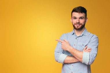 Kollarını kavuşturup, parlak sarı bir arka planın önünde duran bir adam reklam için fotokopi alanını işaret ediyor.