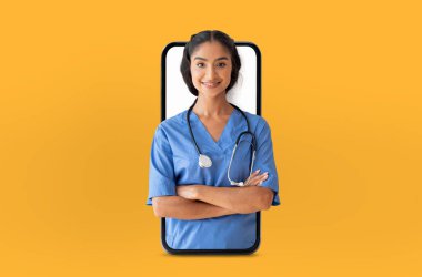 Mavi önlüklü Hintli kadın doktor, kollarını kavuşturmuş, akıllı telefon ekranında, teletıp veya dijital sağlık hizmetleri yeniliklerini sembolize ediyor.