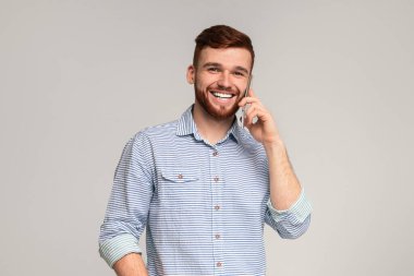 Mutlu Milenyum Adamı Cep Telefonuyla Konuşuyor ve Kameraya Gülümsüyor, gri stüdyo arka planı, serbest alan