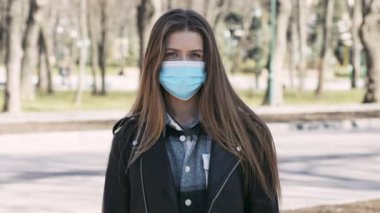 Salgın. Koruyucu maske takan genç bir kadın boş şehir parkında tek başına duruyor.
