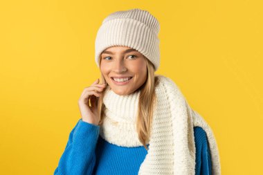 Beyaz şapkalı ve eşarplı bir kadın dışarıda duruyor. Yüzünde tarafsız bir ifadeyle kameraya bakıyor. Şapka başını örtüyor, atkı da boynuna dolanmış.