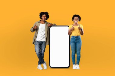 Siyah bir adam ve kadın boş bir ekranın yanında duruyorlar. Kadın beyaz bir elbise giyerken adam siyah bir gömlek giyiyor. Boş ekrana dikkatle bakıyor gibi görünüyorlar..