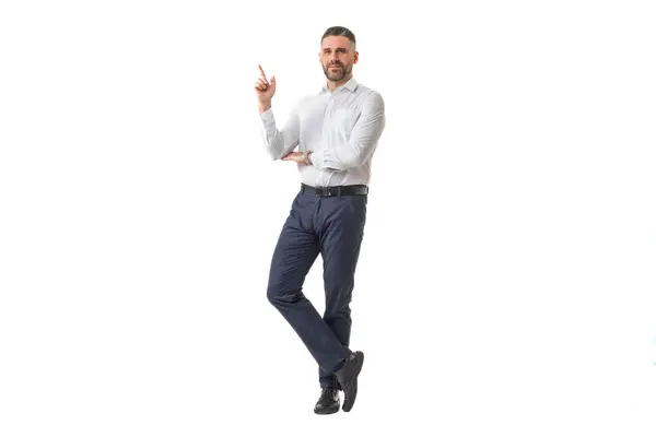stock image A man dressed in a white shirt and black pants poses confidently, pointing upwards with his finger, suggesting an idea or giving advice.