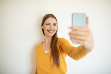 Dışarıda duran bir kız kol mesafesinde bir akıllı telefonu tutuyor, gülümsüyor ve ön kamerayla selfie çekerken poz veriyor..