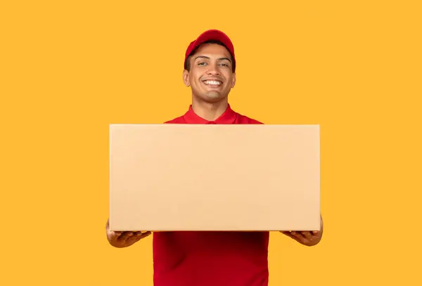 Stock image A man wearing a red shirt is seen grasping a cardboard box in his hands. The man appears to be standing upright, firmly holding onto the box with a focused expression on his face.