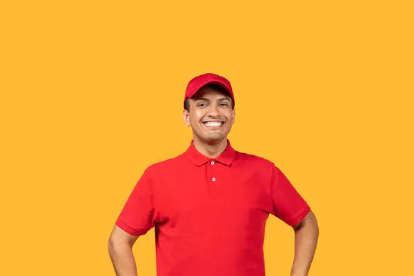 stock image A cheerful man stands with his hands on his hips, wearing a bright red uniform and matching cap, against a vibrant yellow backdrop. He is smiling widely, appearing enthusiastic and approachable.