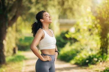 Atletik kadın, elleri kalçasında bir yolda kendinden emin bir şekilde duruyor. Çevresini inceliyor gibi görünüyor. Otorite ve kararlılık hissi yayıyor..