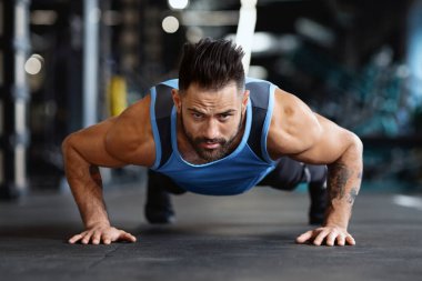 Kolsuz tişört giyen bir adam spor salonunda şınav çeker..