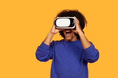 Parlak mavi kazaklı genç bir adam içeride sanal gerçeklik yaşıyor. VR kulaklık kullanırken heyecanlı ve meşgul görünüyor..
