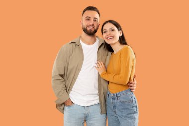 Bir erkek ve bir kadın yan yana duruyorlar, ileriye bakıyorlar. Aynı yöne bakıyor gibi gözüküyorlar. Her iki şahıs da sıradan giyinmiş ve yüzlerinde tarafsız ifadeler var..