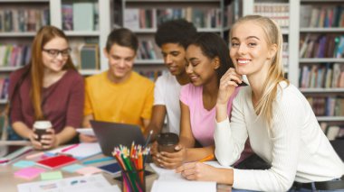 Neşeli Genç Üniversite Öğrencileri KütüphaneDe Birlikte Eğitim Alıyor, dizüstü bilgisayarla çalışıyor ve konuşuyor