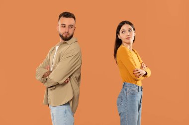 Genç bir erkek ve kadın sırt sırta verip, kollarını kavuşturuyorlar, bu da anlaşmazlık ya da anlaşmazlığa işaret ediyor. Arkaplan turuncu renkte.