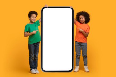 İki Afrikalı Amerikalı çocuk dev bir akıllı telefonun önünde duruyor, yüzlerindeki gülümsemeyle boş ekrana bakıyorlar..