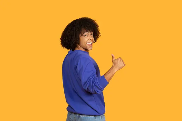 stock image A man wearing a blue shirt and jeans stands in the image, enthusiastically giving a thumbs up gesture. His casual attire and positive expression convey a sense of approval and happiness.