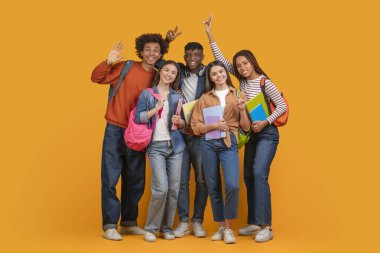 Bu resim, bir grup farklı öğrencinin parlak sarı bir arkaplan önünde gülümseyip poz verdiklerini gösteriyor. Hepsi kitap tutuyor ve sırt çantası takıyorlar.
