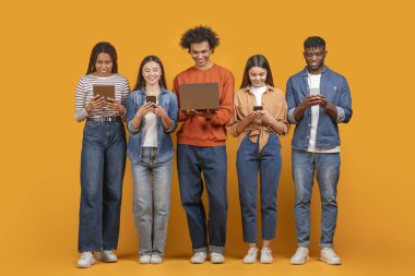 Bu resim, sarı arka planda sıralanmış beş genç yetişkinden oluşan bir grubu gösteriyor. Hepsi, bir tablet, bir akıllı telefon ve bir dizüstü bilgisayar içeren cihazlarına bakıyor.