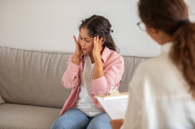 Bir kadın kanepeye oturur, kafası ellerinin arasındadır, terapi seansı sırasında endişeli görünür. Terapist onun yanında oturuyor, endişeli görünüyor..
