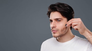 Yakışıklı adam yüzüne nemlendirici serum uygulayarak, gri stüdyo arka plan